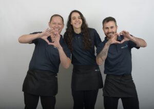 Three smiling We Clean It employees make a heart gesture toward clients, radiating positivity and peace of mind.